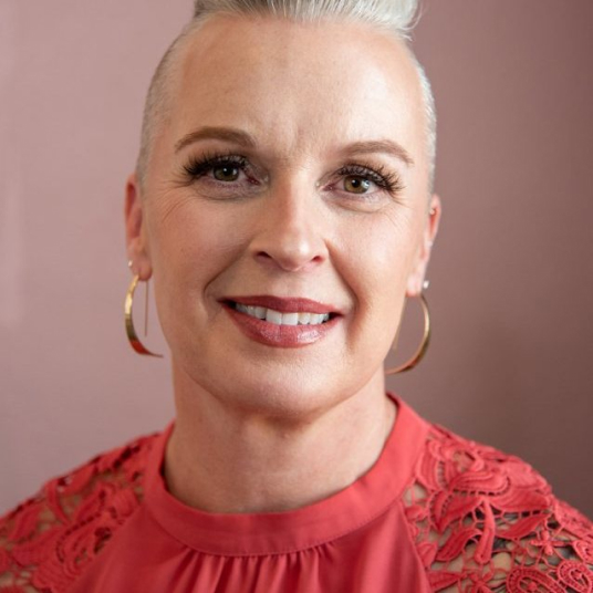 A woman in a red top with a shaved head.