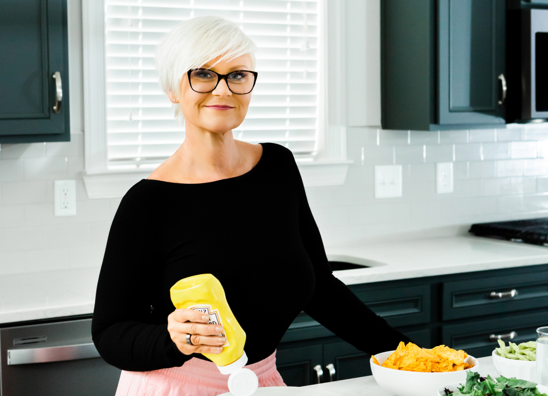 A woman in glasses standing in front of a kitchen counter.