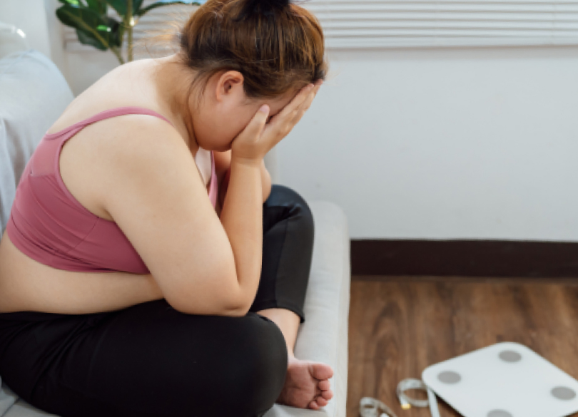 Woman on a couch crying next to a scale