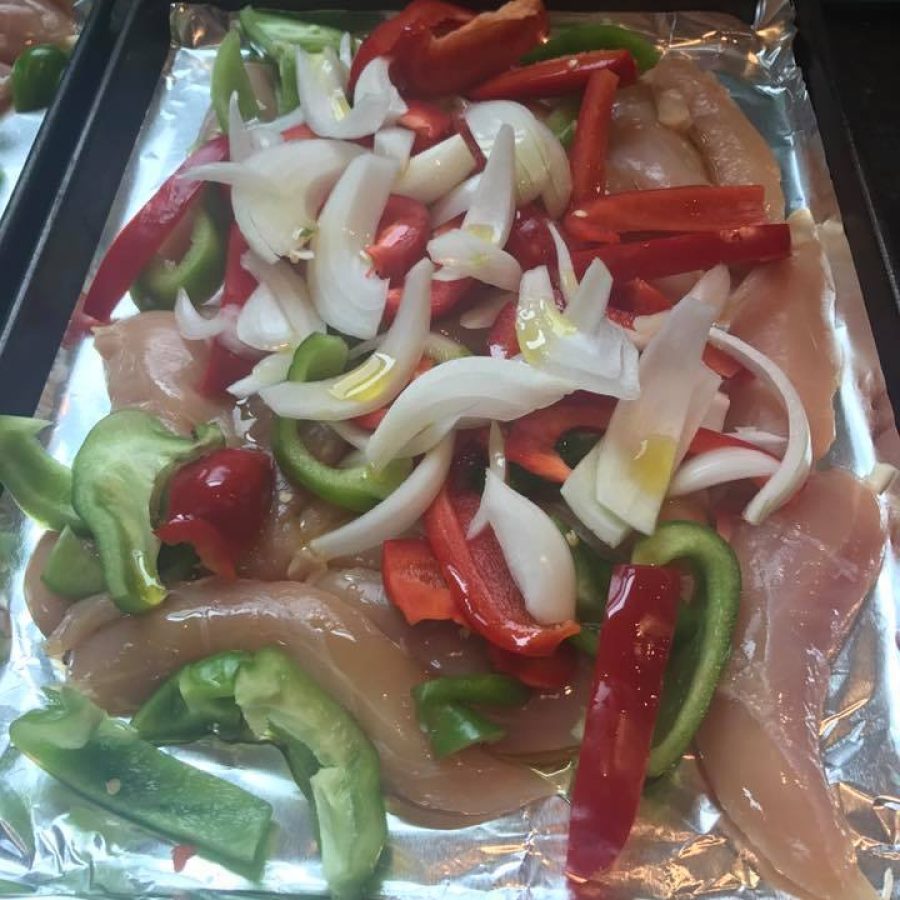A sheet of foil with chicken, peppers and onions on it.